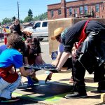 A group of people lay a carving down the ground to be steamrolled.