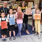 A group of five kids and two adults hold their prints up.