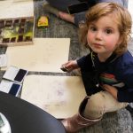 A young kid looks up while stamping a piece of paper.