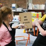 A kid points to a sign being held by an adult.