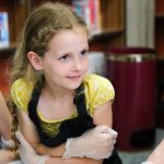 A girl wearing an apron and plastic gloves.