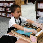 A boy rolls out his letterpress print.